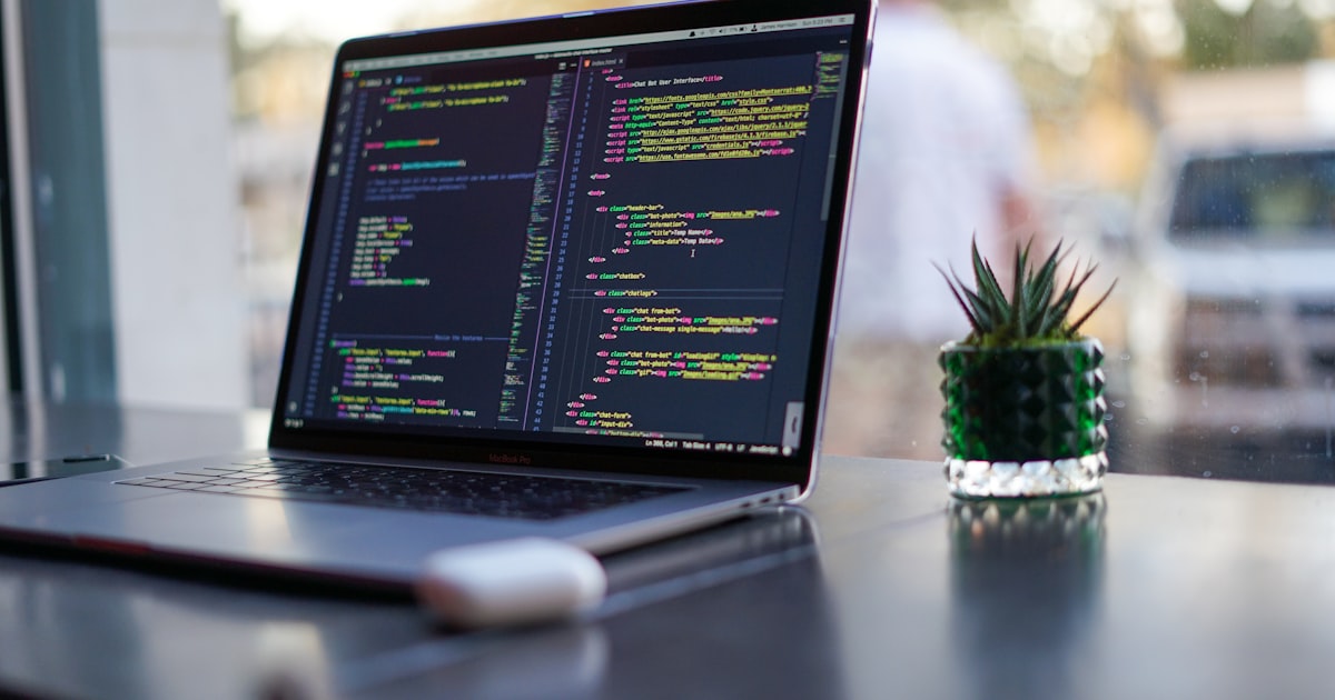 Ordinateur portable ouvert sur du code d'application web, posé près d'une fenêtre